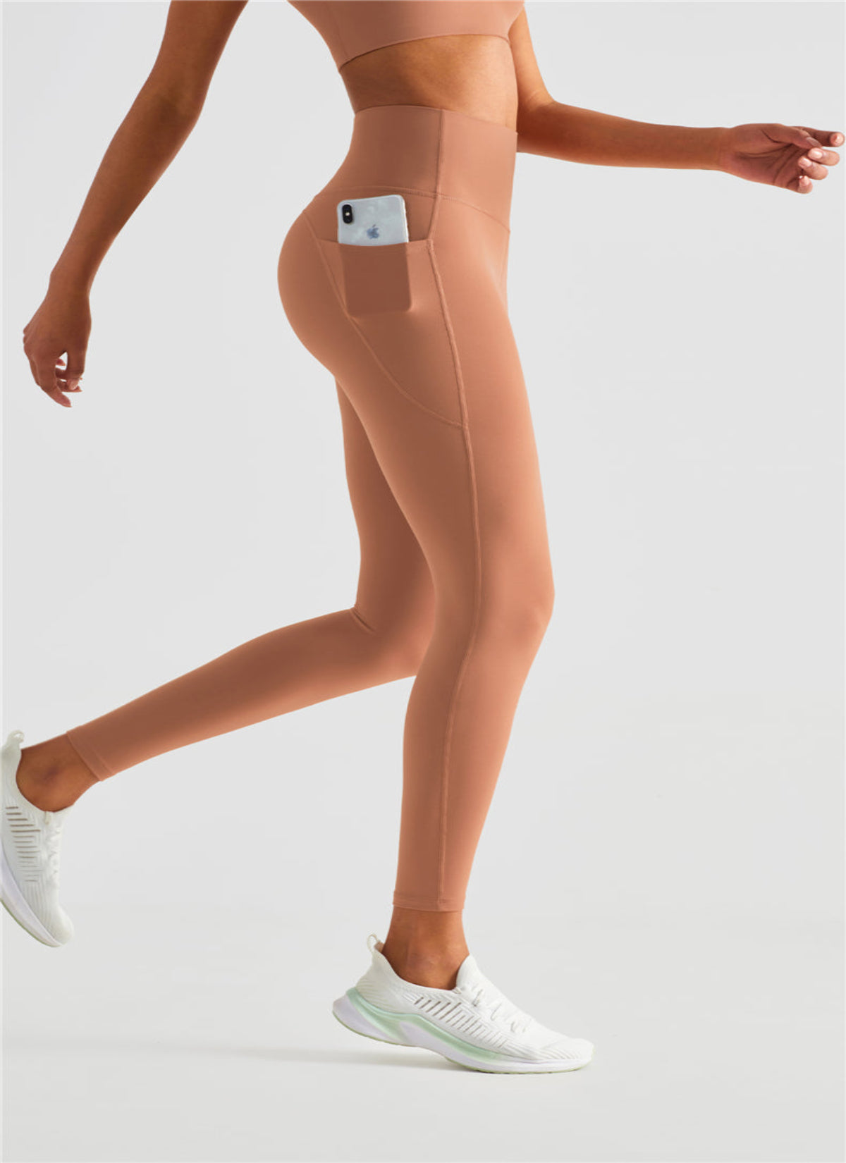 Person wearing peach leggings with a pocket on a light gray background
