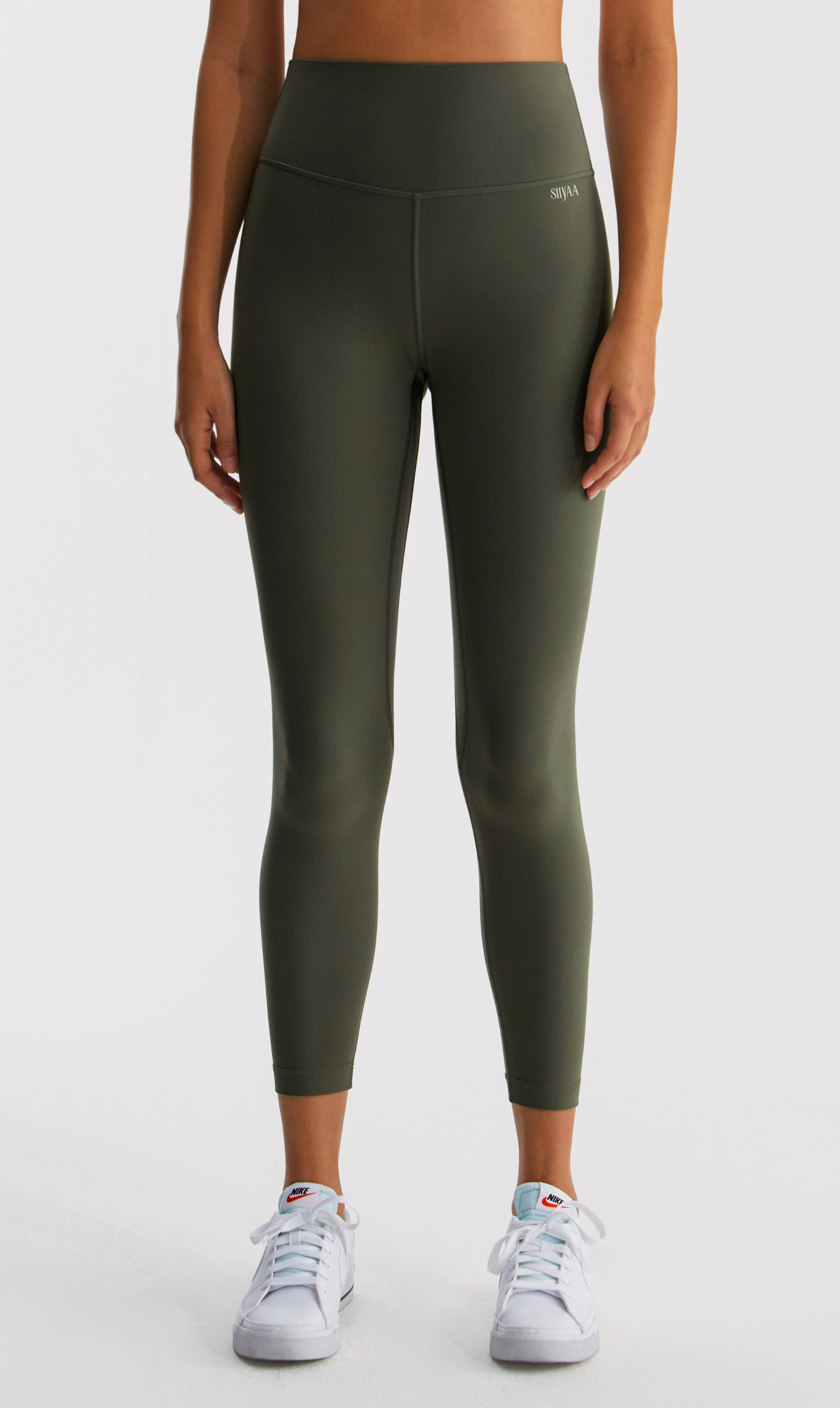 Woman wearing a white sports bra and green leggings on a white background