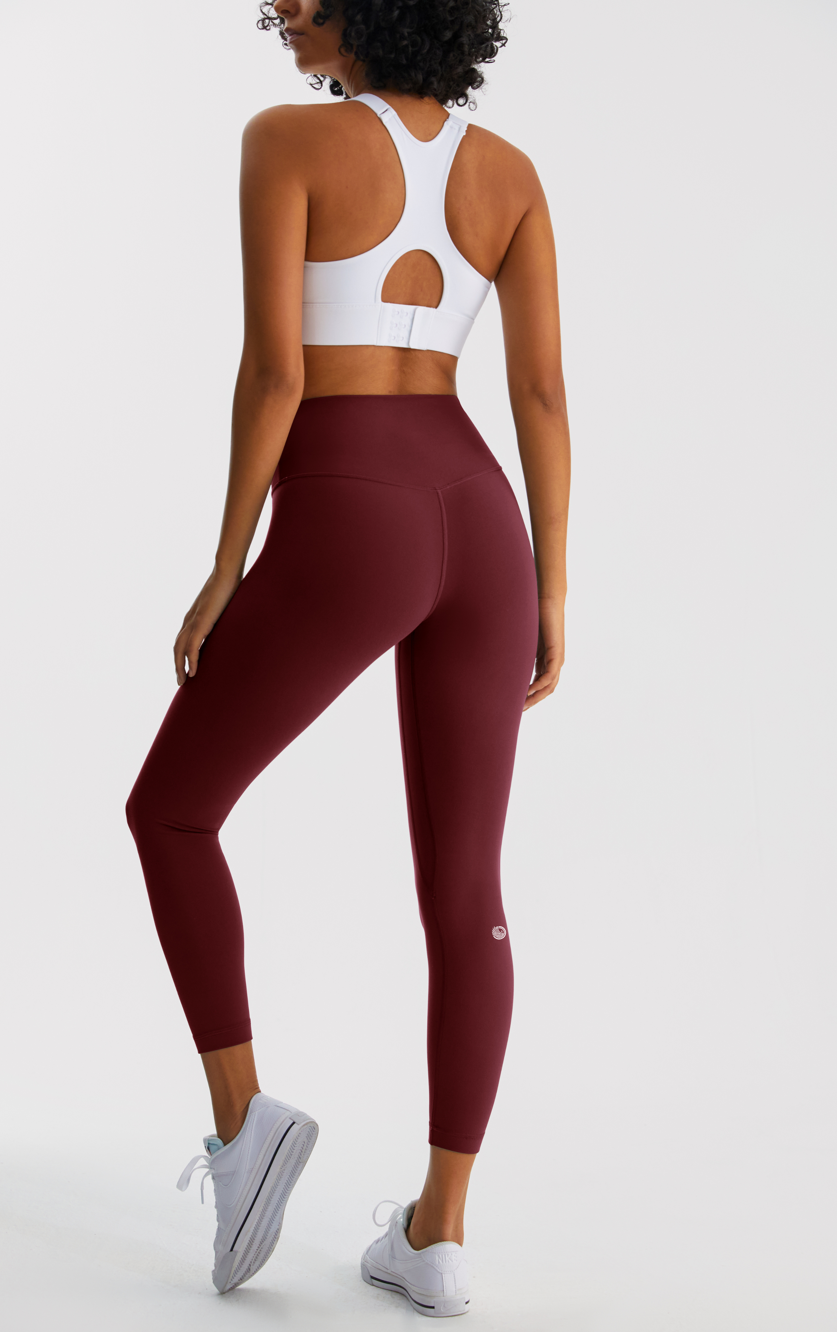 Person wearing maroon leggings and a white sports bra on a light gray background